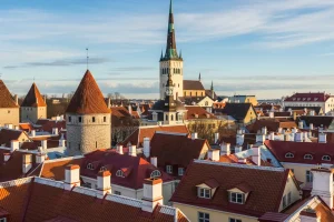A view of the iconic red rooftops of Tallinn's Old Town with a medieval spire against a blue sky