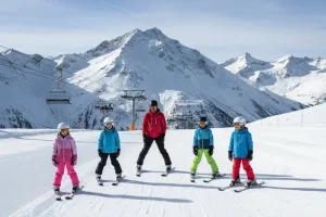 A small group of beginner skiers practicing the snowplough technique on a very wide, gentle, and well-groomed blue slope high in the Austrian Alps, guided by an instructor and demonstrating a safe learning environment.