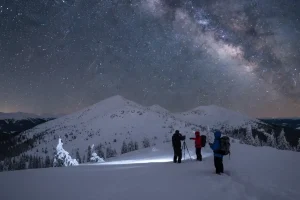 A brilliant, clear night sky filled with countless stars over a snowy mountain range