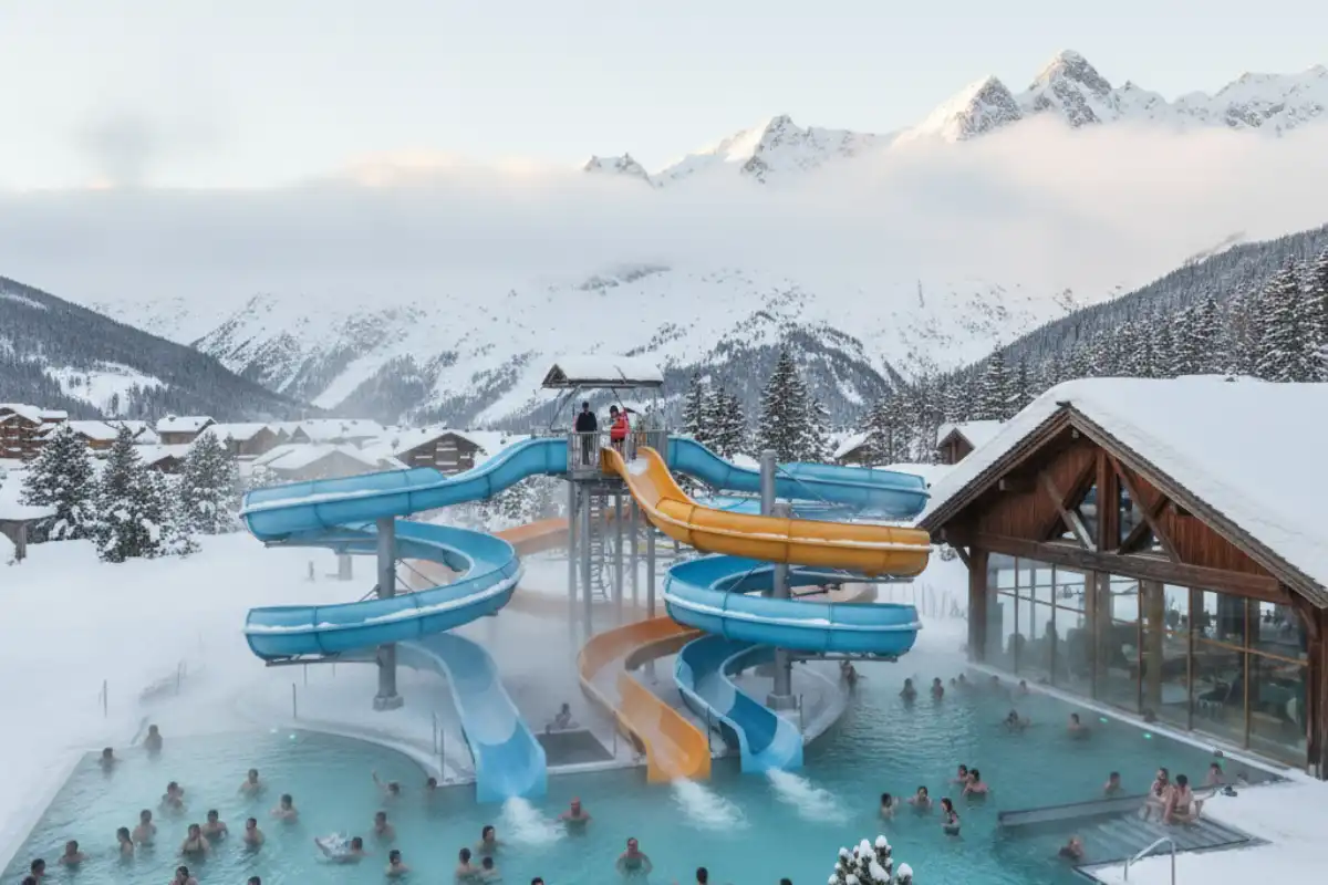 People enjoying the heated outdoor pools and water slides at the Aquariaz water park in Avoriaz with snow visible outside.