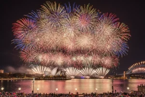 Spectacular fireworks exploding over a famous global landmark, surrounded by a massive crowd celebrating, capturing the electrifying energy of a major New Year's Eve city party.