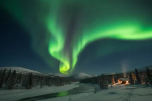 Intense green Aurora Borealis dancing across the dark sky above a tranquil, snow-covered landscape