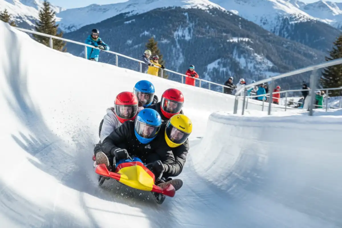 A group of people enjoying a high-speed ride down the Olympic Bobsleigh run in La Plagne, wearing helmets and smiling.