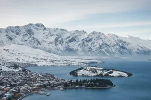 A scenic view of Queenstown town centre nestled beside Lake Wakatipu, surrounded by snowy mountains in the winter.