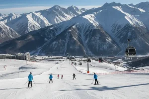 A panoramic view of Shymbulak Ski Resort with wide, groomed slopes and the jagged peaks of the Tien Shan Mountains in the background.