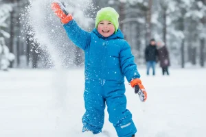 A smiling child wearing bright blue waterproof snow gear playing cheerfully in fresh powder snow