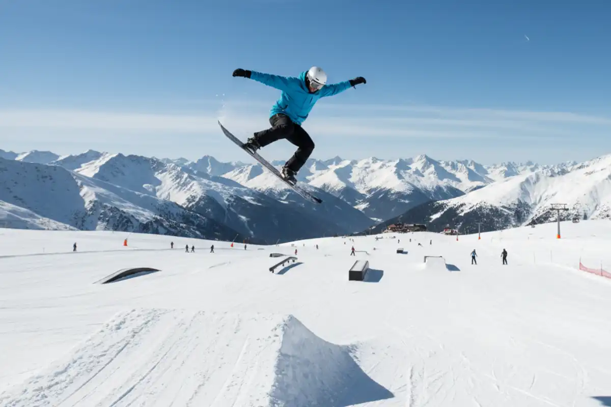 A snowboarder launching off a small kicker in the Baqueira-Beret snowpark with clear blue skies.
