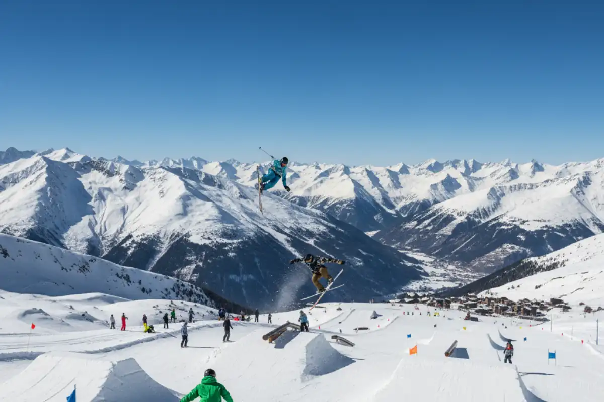 Snowboarders and skiers hitting jumps and rails in the large, well-maintained snowpark on the glacier of Les Deux Alpes.