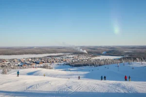 The wide, smooth slopes of Ylläs in Finnish Lapland under the blue Arctic sky, with the village of Äkäslompolo visible below.