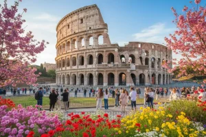 The Roman Colosseum framed by blooming spring flowers under a clear blue sky.