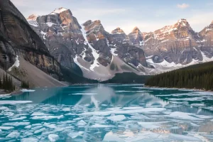 Snow-capped mountain peaks reflecting in the partially thawed turquoise waters of a glacial lake during the early Canadian spring