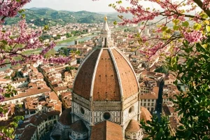Aerial view of the terracotta-domed Florence Cathedral framed by pink spring blossoms and lush greenery