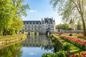 The majestic Château de Chenonceau arching over the Cher River surrounded by vibrant green spring foliage and tulip beds