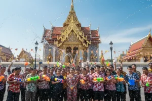 People joyfully splashing water during the Songkran festival in front of a traditional golden Thai temple under the bright April sun