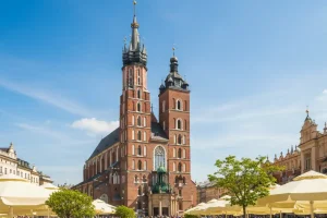 The iconic towers of St. Mary's Basilica in Krakow rising above the Main Market Square filled with white umbrellas of open-air cafes and early spring greenery