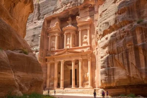 The iconic Treasury of Petra carved into sandstone cliffs framed by narrow rock walls under a bright spring sun