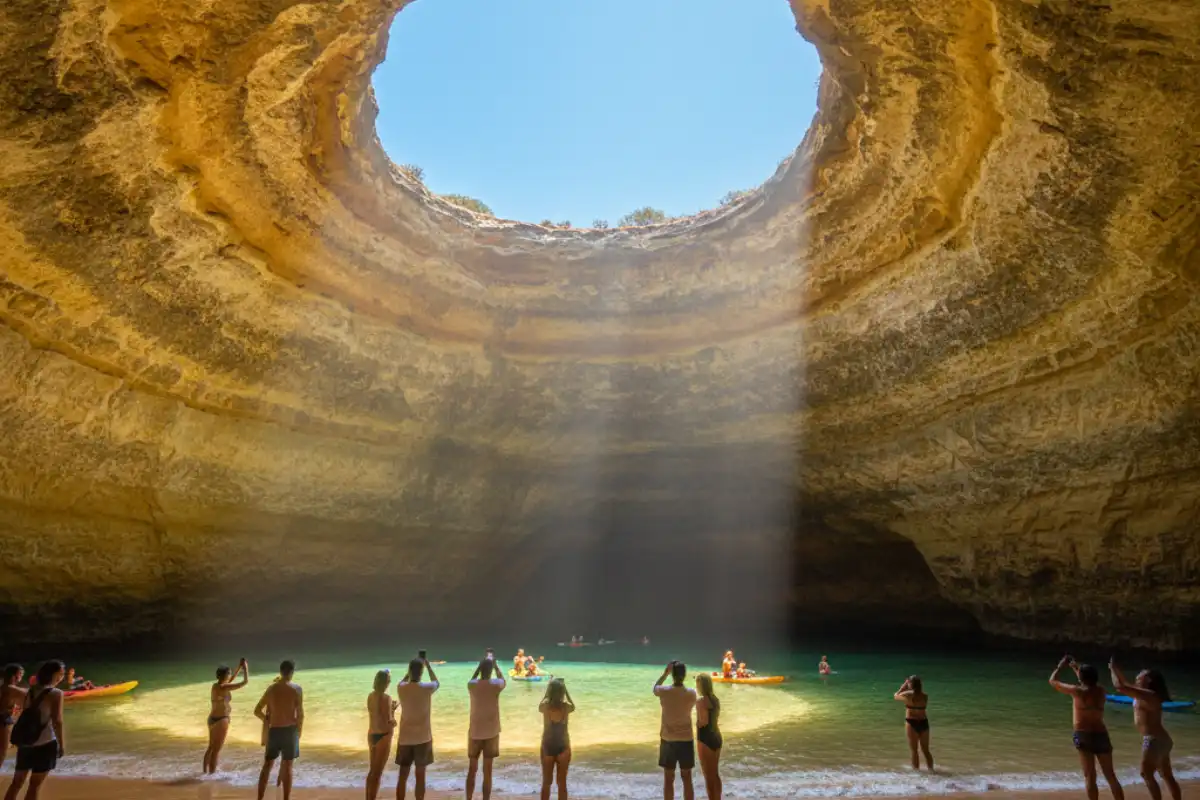 Looking up from the sand inside the Benagil sea cave at the circular opening in the ceiling revealing a bright blue sky