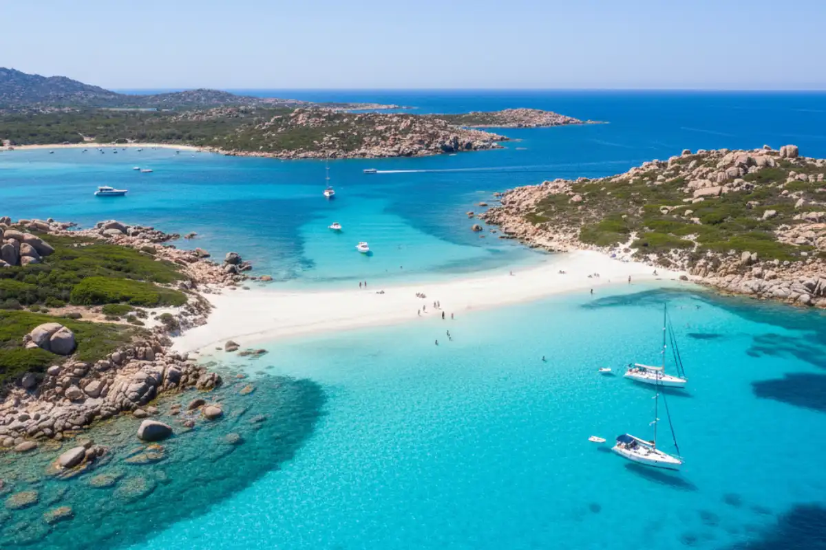 A bird's-eye view of a white sandbar stretching between two islands in the La Maddalena Archipelago with navy and cyan water